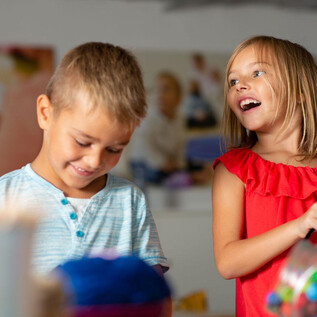 Two children are having fun and laughing together. The boy is wearing a light blue shirt and the girl a red dress. | © Hannelore Kirchner