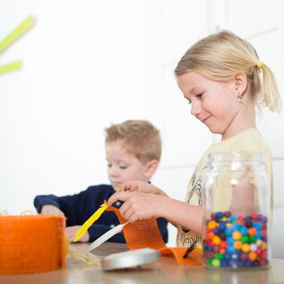Zwei Kinder arbeiten kreativ an einem Tisch. Eines der Kinder schneidet orangefarbenes Material, während das andere mit bunten Perlen spielt. | © Hannelore Kirchner