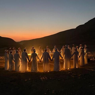 Eine Gruppe von Menschen steht im Kreis und hält sich an den Händen. Im Hintergrund ist ein malerischer Sonnenuntergang zu sehen. | © Kareem Gamal