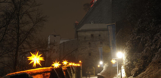 A romantic night shot of a castle with snow-covered paths. Lights in the shape of stars illuminate the surroundings and create a festive atmosphere. | © Salzburger Burgen und Schlösser