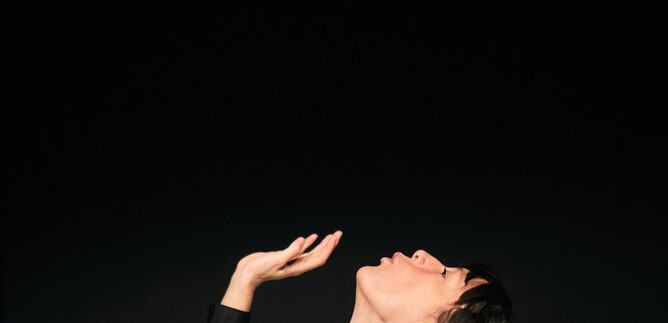 A person looks up and holds their hand raised. Above them hovers a pink object against a dark background. | © Siegrid_Cain