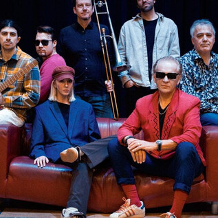 Skupina hudebníků pózuje na pohovce. Ukazují různé oblečení a drží nástroje v ruce. | © Jazzit