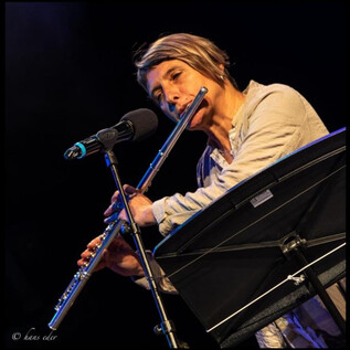Une musicienne joue de la flûte sur scène. Elle se tient devant un microphone et se concentre sur son jeu. | © Hans Eder