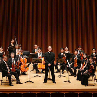 Un orchestre est sur une scène. Le chef d'orchestre se tient devant, entouré de musiciens avec différents instruments. | © COLUMBUS Reisen GmbH & Co.KG