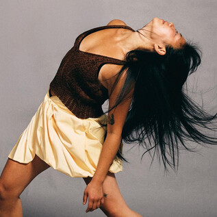 Egy táncoló nő hosszú hajjal és egy ruhában. Dinamikusan mozog egy szürke háttér előtt. | © Chris Rogl