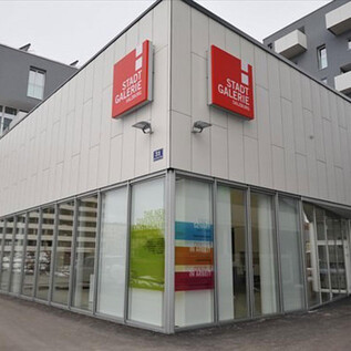 Una moderna instalación comercial con grandes ventanales de vidrio. El edificio lleva un cartel rojo con la inscripción "Galería de la Ciudad". | © Stadtgemeinde Salzburg
