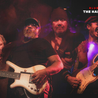 Egy zenekar élőben játszik a színpadon. A zenészek szenvedélyes kifejezésekkel a kezükben tartják hangszereiket. | © mike catches light