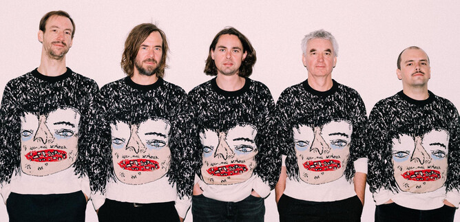 Five men stand next to each other wearing eye-catching sweaters featuring an artistic face. The background is kept bright and neutral. | © Ingo Pertramer