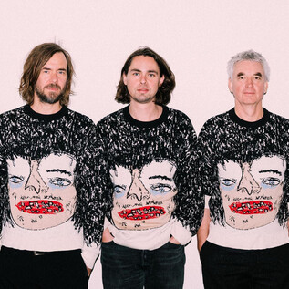 Fünf Männer stehen nebeneinander und tragen auffällige Pullover mit einem künstlerischen Gesicht. Der Hintergrund ist hell und neutral gehalten. | © Ingo Pertramer