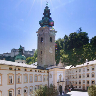 Ein historisches Gebäude mit einem markanten Turm und schönem grünen Hintergrund. Der Himmel ist klar und sonnig, was die Architektur hervorhebt. | © Erzabtei St. Peter