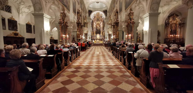 Una magnifica chiesa con una bella volta e molti dettagli decorativi.  
Molte persone sono sedute nei banchi e ascoltano un evento. | © Erzabtei St. Peter