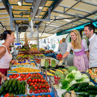 Ein lebhafter Markt mit frischem Obst und Gemüse. Zwei Kunden unterhalten sich freundlich mit einer Verkäuferin. | © Tourismus Salzburg GmbH, Breitegger G.