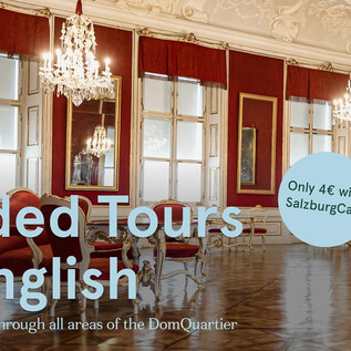 An elegant room with crystal chandeliers and large windows. There is information about guided tours in English at the DomQuartier.