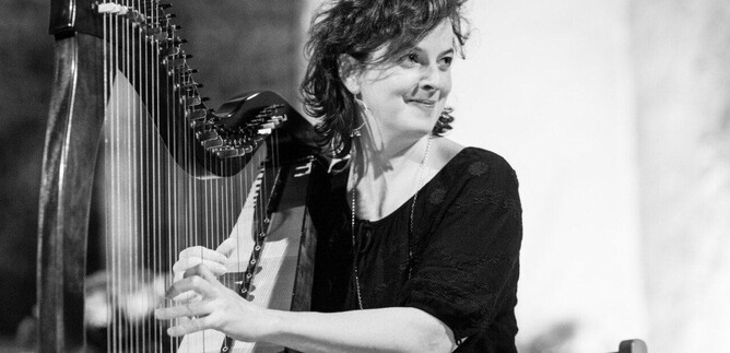Eine Frau spielt Harfe und lächelt dabei. Der Hintergrund ist unscharf und trägt zur musikalischen Atmosphäre bei. | © Weltenklang