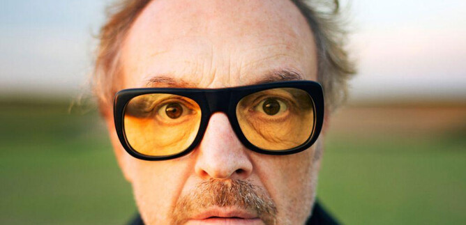 Muž s brýlemi a stylovým účesem se dívá přímo do kamery. V pozadí je vidět zelená krajina. | © www.lukasbeck.com