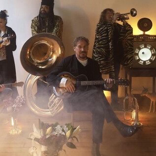 Kapela hraje v místnosti, zatímco se vytváří mystická atmosféra s mlhou a jemnými světly. V popředí sedí hudebník s kytarou a ostatní instrumentalisté stojí v pozadí. | © Agentur/Band