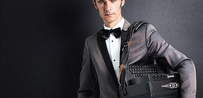 An elegantly dressed man in a tuxedo holds an accordion. The background is dark, which focuses attention on him and his instrument. | © Günther Egger