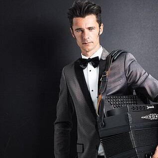 An elegantly dressed man in a tuxedo holds an accordion. The background is dark, which focuses attention on him and his instrument. | © Günther Egger
