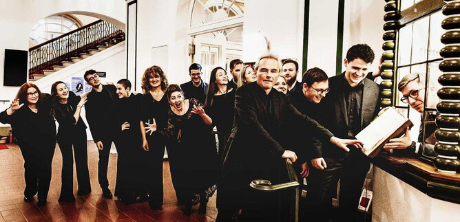 A group of people in formal clothing stands in a hallway and smiles. They seem to be waiting for something and have a cheerful atmosphere. | © Mario Balzi