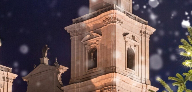 Una hermosa torre iluminada por la noche, rodeada de copos de nieve. En el primer plano se puede ver un árbol de Navidad. | © Universität Mozarteum