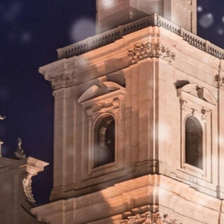 Una hermosa torre iluminada por la noche, rodeada de copos de nieve. En el primer plano se puede ver un árbol de Navidad. | © Universität Mozarteum