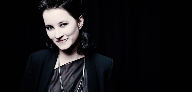A woman with dark hair smiles at the camera. The background is black, which draws the focus to her face. | © Marco Borggreve