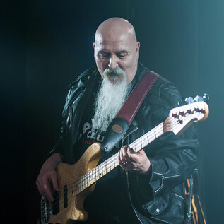 A musician is playing bass on stage. He is wearing a leather jacket and has a long white beard. | © Rockhouse Salzburg