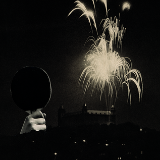 A hand holds a table tennis racket against a night sky with fireworks. In the background, a silhouette of buildings is seen out of focus. | © Sammlung Generali Foundation