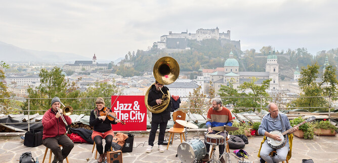 A jazz band is playing at a viewpoint overlooking the city. In the background, a castle and a beautiful landscape can be seen. | © )Henry Schulz
