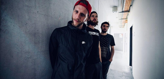 Three young men are standing in a long, bright hallway. The walls are gray and designed in a minimalist style. | © Jazzit