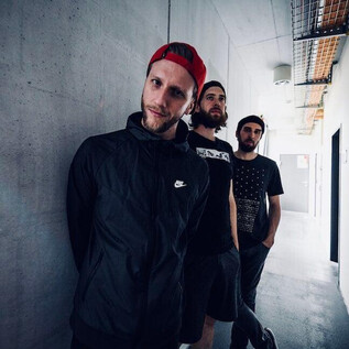 Three young men are standing in a long, bright hallway. The walls are gray and designed in a minimalist style. | © Jazzit