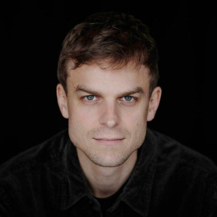 Un portrait d'un homme avec les cheveux courts et une expression neutre. L'arrière-plan est sombre, ce qui attire l'attention sur son visage. | © Jazzit_Max Santner