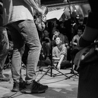 Une formation de jazz joue en direct sur une scène. En arrière-plan, des auditeurs enthousiastes sont assis et écoutent la musique. | © Jazzit