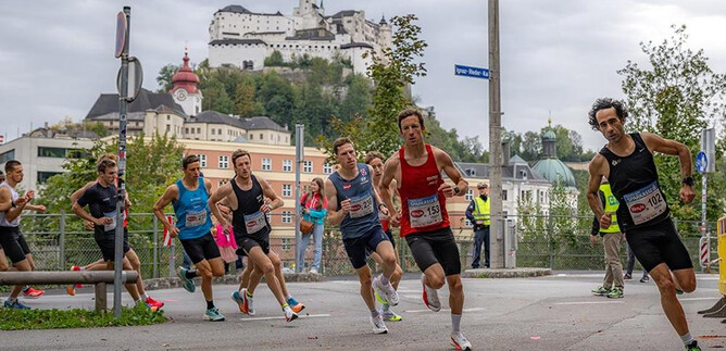 A group of runners is participating in a race, while an impressive castle can be seen in the background. The atmosphere is sporty and dynamic. | © Jedermannlauf