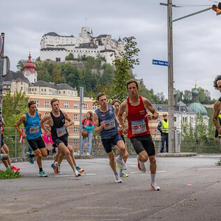 A group of runners is participating in a race, while an impressive castle can be seen in the background. The atmosphere is sporty and dynamic. | © Jedermannlauf