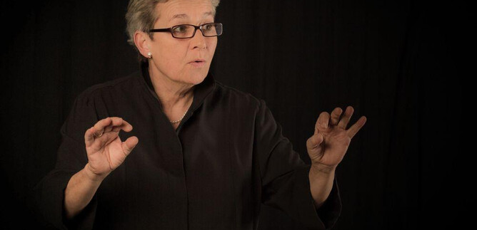 A woman stands in the foreground and speaks passionately. In the background, a dark fabric is visible. | © Wali.pix