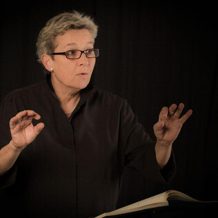 A woman stands in the foreground and speaks passionately. In the background, a dark fabric is visible. | © Wali.pix