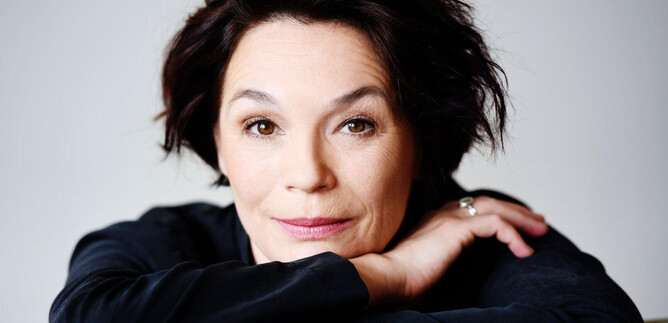 A portrait of a woman with dark, curly hair. She looks directly at the camera and radiates a friendly demeanor. | © Miriam Knickriem