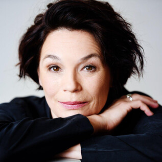 Ein Porträt einer Frau mit dunklen, lockigen Haaren. Sie schaut direkt in die Kamera und strahlt eine freundliche Ausstrahlung aus. | © Miriam Knickriem