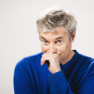 Un uomo con i capelli biondi indossa un maglione blu.   
Guarda con un'espressione pensierosa direttamente nella telecamera. | © Moritz Schell