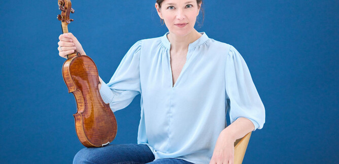 Žena sedí na židli a drží v ruce housle. Pozadí je modré a žena má na sobě světle modrou blůzu. | © Kaupo Kikkas