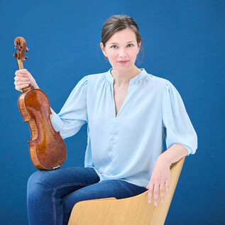 Une femme est assise sur une chaise et tient un violon dans la main. L'arrière-plan est bleu et la femme porte un haut bleu clair. | © Kaupo Kikkas