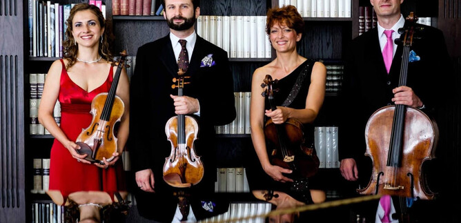 Stringové kvarteto stojí před knihovnou. Všichni hudebníci drží své nástroje a přátelsky se dívají do kamery. | © Tomasz Trzebiatowski