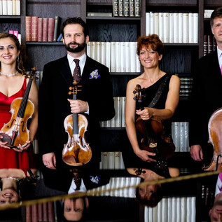 A string quartet stands in front of a bookshelf. All the musicians are holding their instruments and looking pleasantly at the camera. | © Tomasz Trzebiatowski