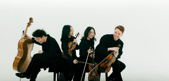 Skupina čtyř hudebníků sedí oblečena v černé. Hrají na různé smyčcové nástroje a působí přitom veselým dojmem. | © Co Merz