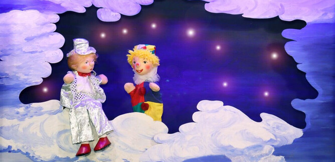 Zwei bunte Puppen sitzen in einer Wolkenlandschaft. Der Hintergrund ist dunkel mit funkelnden Sternen. | © Friedburger Puppenbühne