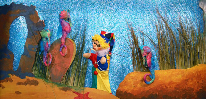 Eine bunte Unterwasserwelt mit einem Puppenspieler und bunten Seepferdchen. Im Hintergrund sind Algen und sandige Unterwasserlandschaften zu sehen. | © Friedburger Puppenbühne