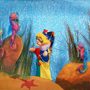 Eine bunte Unterwasserwelt mit einem Puppenspieler und bunten Seepferdchen. Im Hintergrund sind Algen und sandige Unterwasserlandschaften zu sehen. | © Friedburger Puppenbühne