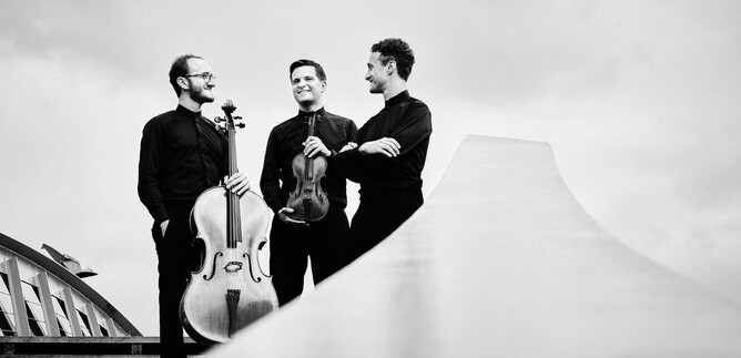 Tre musicisti sono su una scala e sorridono. Uno tiene un violoncello, mentre gli altri tengono un violino e un altro strumento. | © Kaupo Kikkas