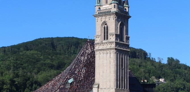 An impressive church with a tall tower rises above the city. In the background, gentle hills and a blue sky are visible.